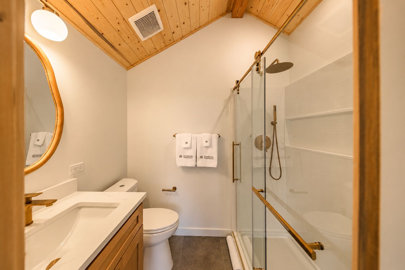 Une salle de bain moderne avec un plafond en bois, une douche en verre, des toilettes blanches et un meuble-lavabo avec un miroir.