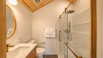 Une salle de bain moderne avec un plafond en bois, une douche en verre, des toilettes blanches et un meuble-lavabo avec un miroir.