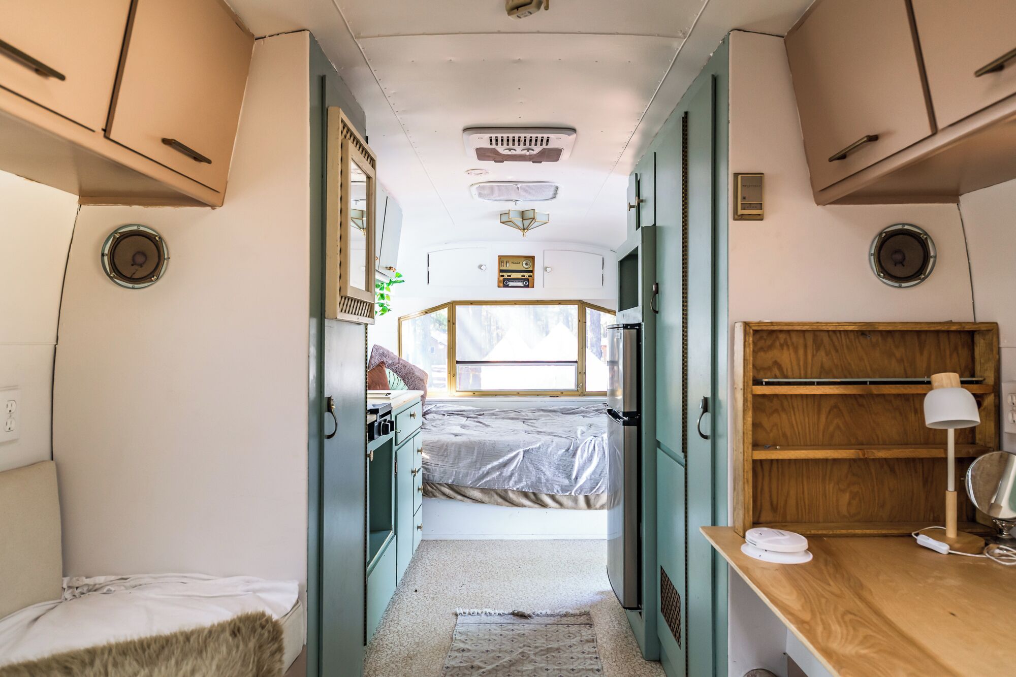 Een compact camperinterieur met een bed, een kitchenette en een klein bureau.