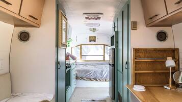 Een compact camperinterieur met een bed, een kitchenette en een klein bureau.