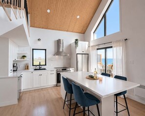 A modern kitchen with a large island, white cabinetry, and a view of the sea.