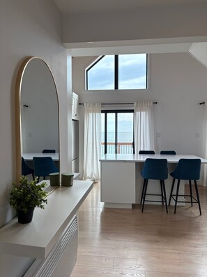 Eine moderne Küche mit einer großen Kochinsel, blauen Barhocker und Meerblick durch ein großes Fenster.
