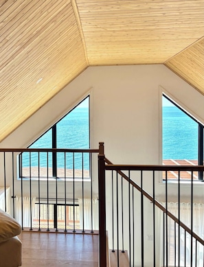Una habitación con techo inclinado, ventanas amplias y vista al mar.