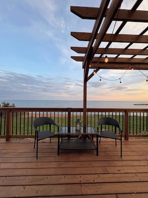 Eine Holzterrasse mit Tisch und StĂŒhlen mit Blick auf einen Strand.