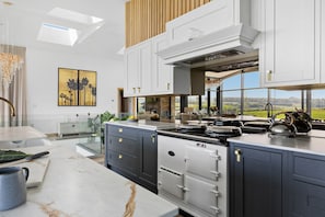 A modern kitchen with a large island, built-in oven, and a view of the countryside. - The Retreat (Ivybridge)