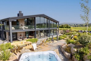 A modern two-story house with a glass facade, outdoor seating, and a hot tub. - The Retreat (Ivybridge)