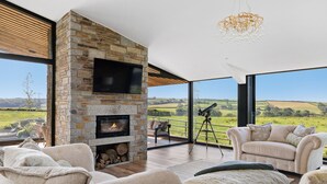 Ein modernes Wohnzimmer mit Kamin aus Stein, großen Fenstern und Blick auf die Landschaft.