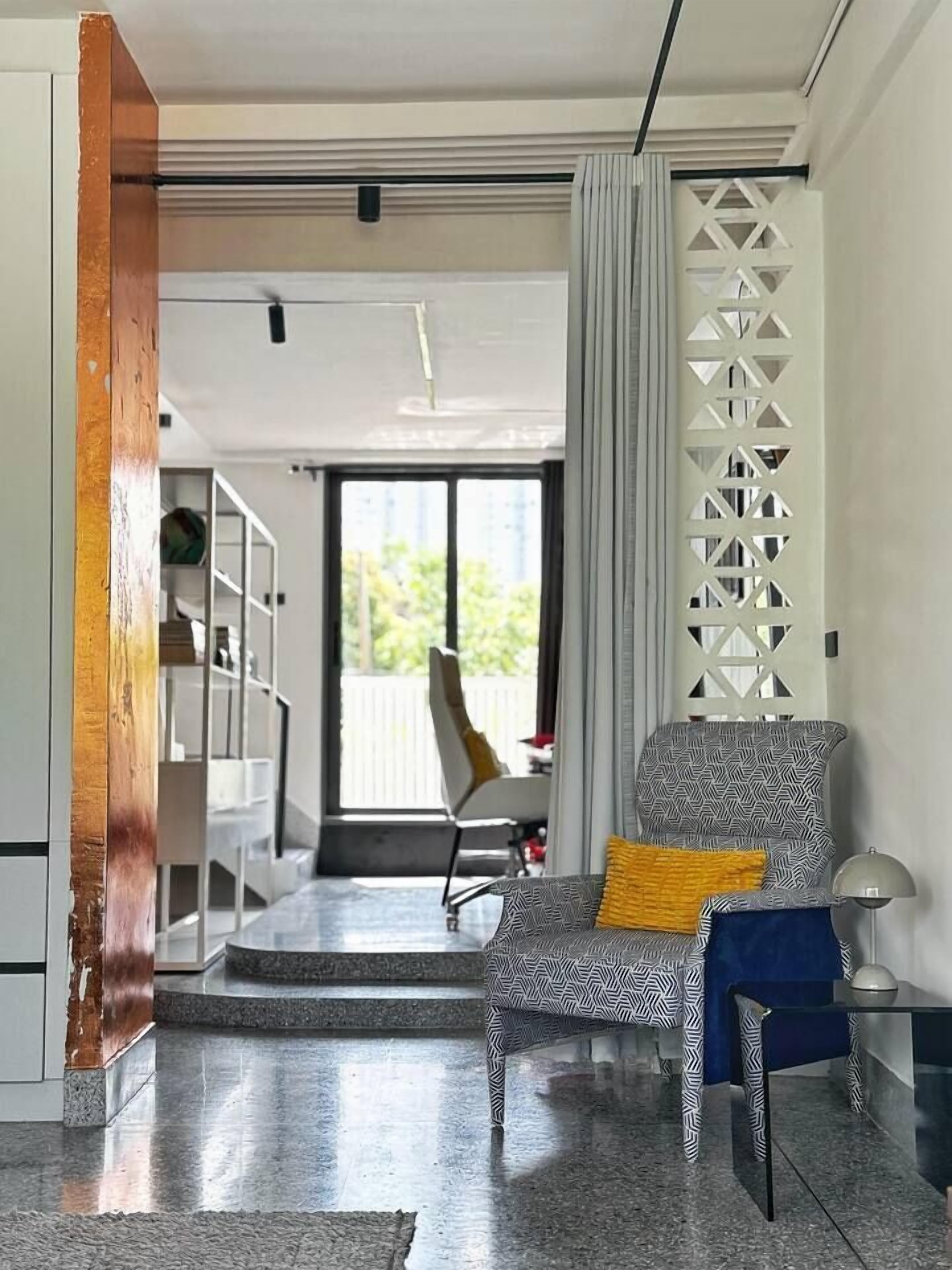 Un salon moderne avec un fauteuil à motifs, une table basse en verre et une vue sur l’extérieur.