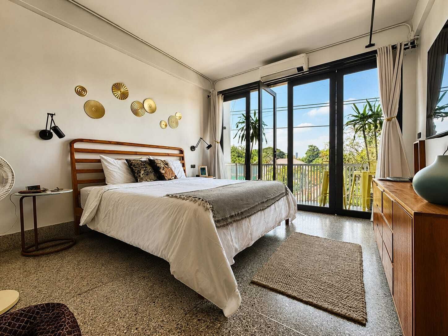 A bedroom with a bed, bedside table, lamp, and a view of the outdoors.
