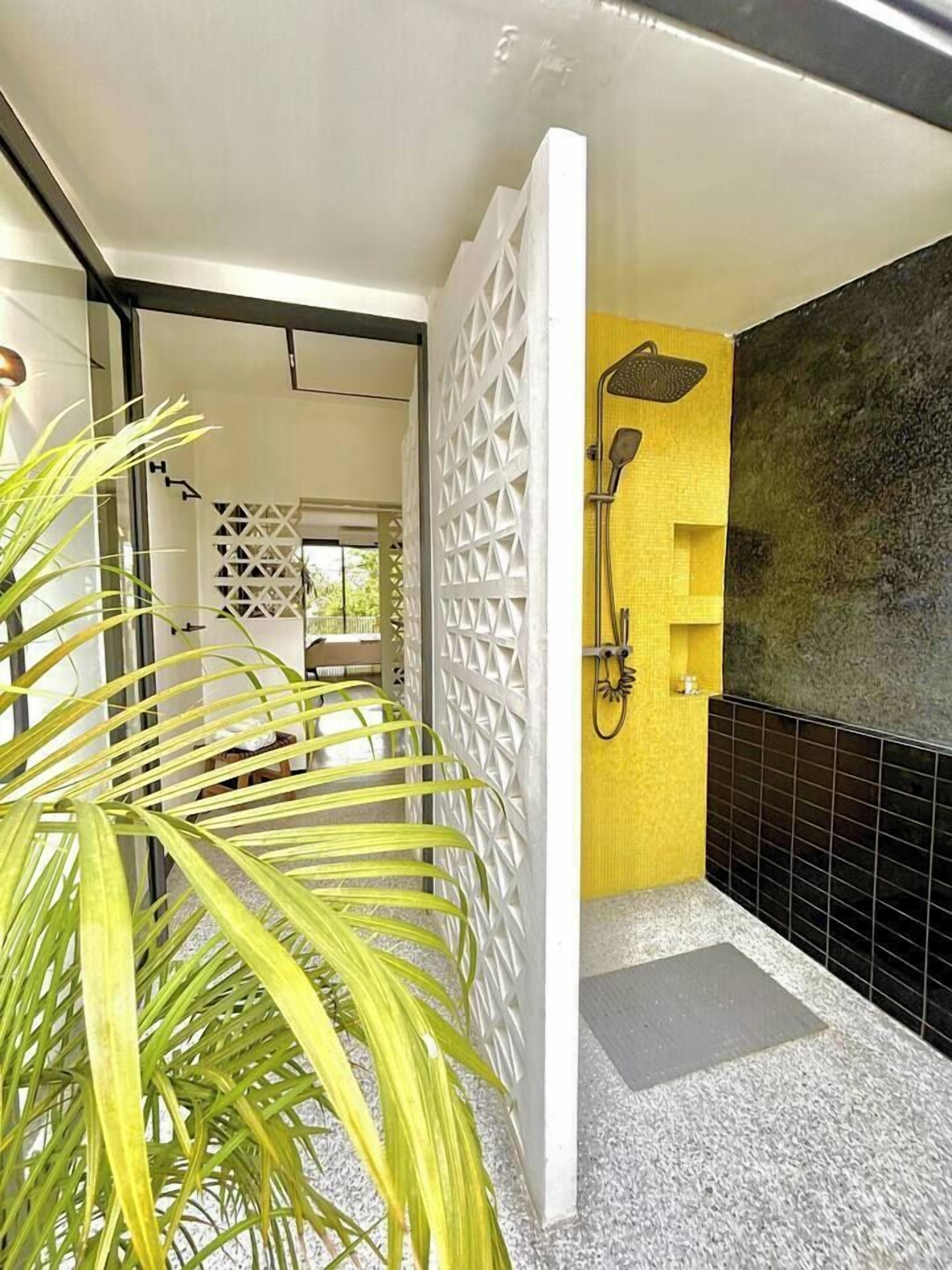 A modern bathroom with a shower, a yellow accent wall, and a white decorative partition.