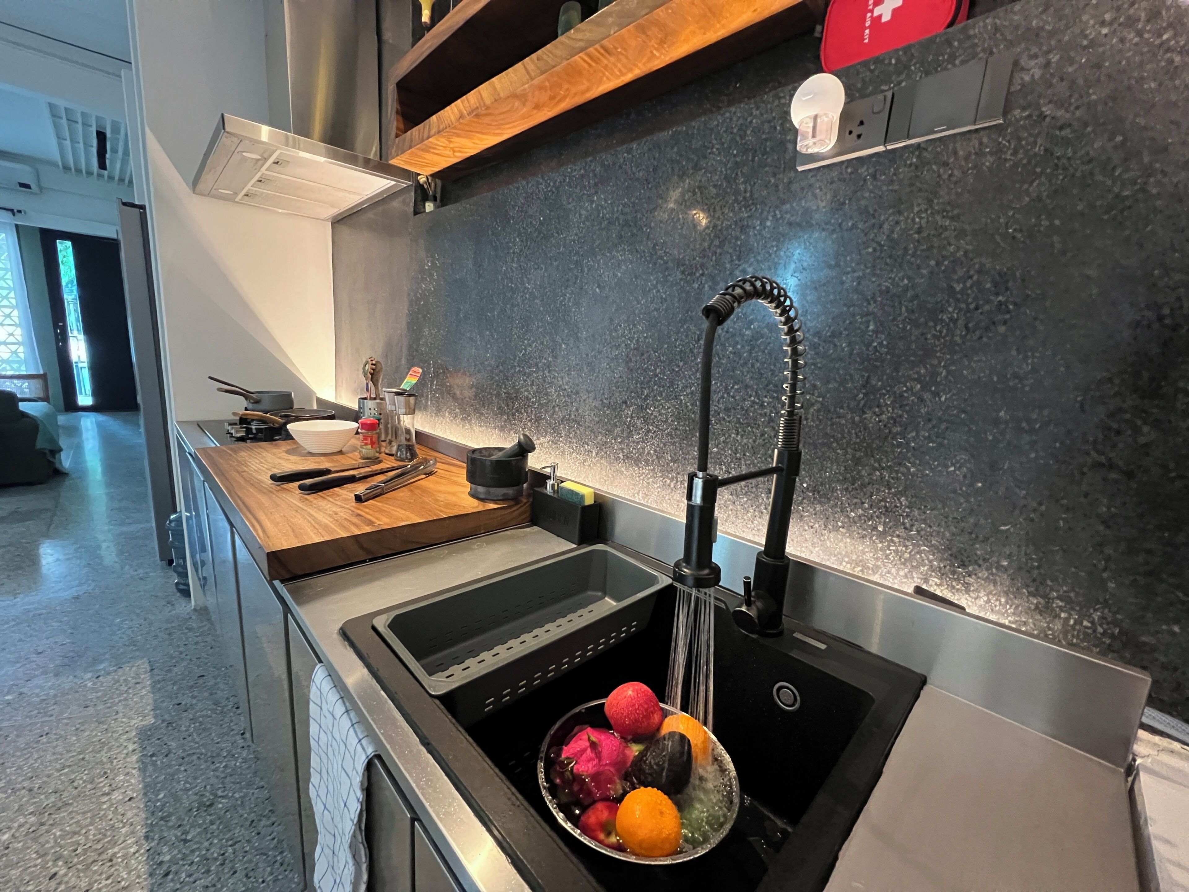 A modern kitchen with a stainless steel sink, wooden countertop, and a fruit bowl.