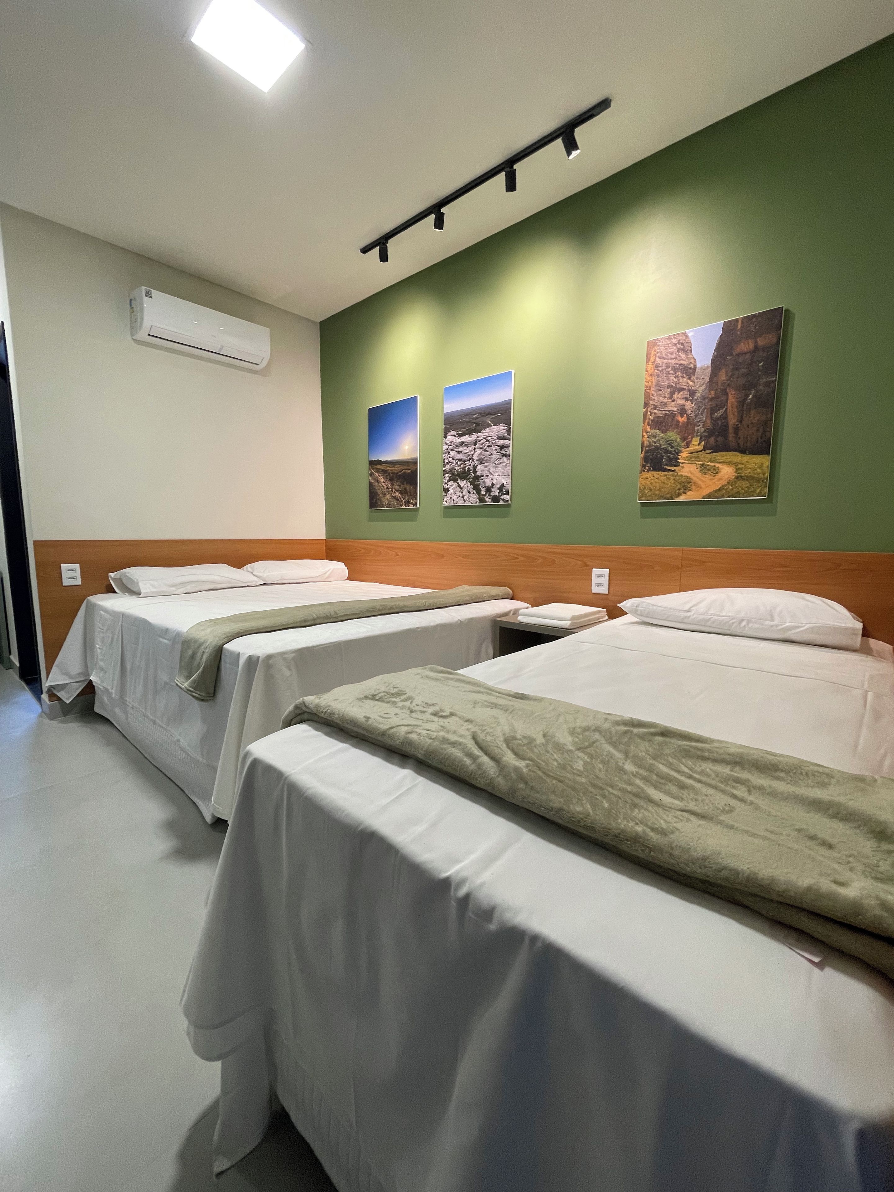Ett hotellrum med tre sängar, en grön vägg och tre inramade tavlor.