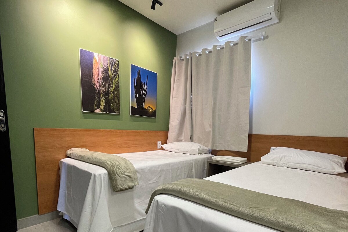 A hotel room with two single beds, a wooden headboard, an air conditioning unit, and two wall-mounted pictures.
