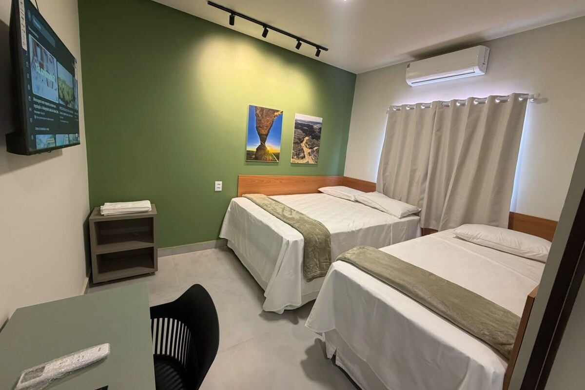 A room with three beds, a desk, a chair, a shelf, and a wall-mounted air conditioner.