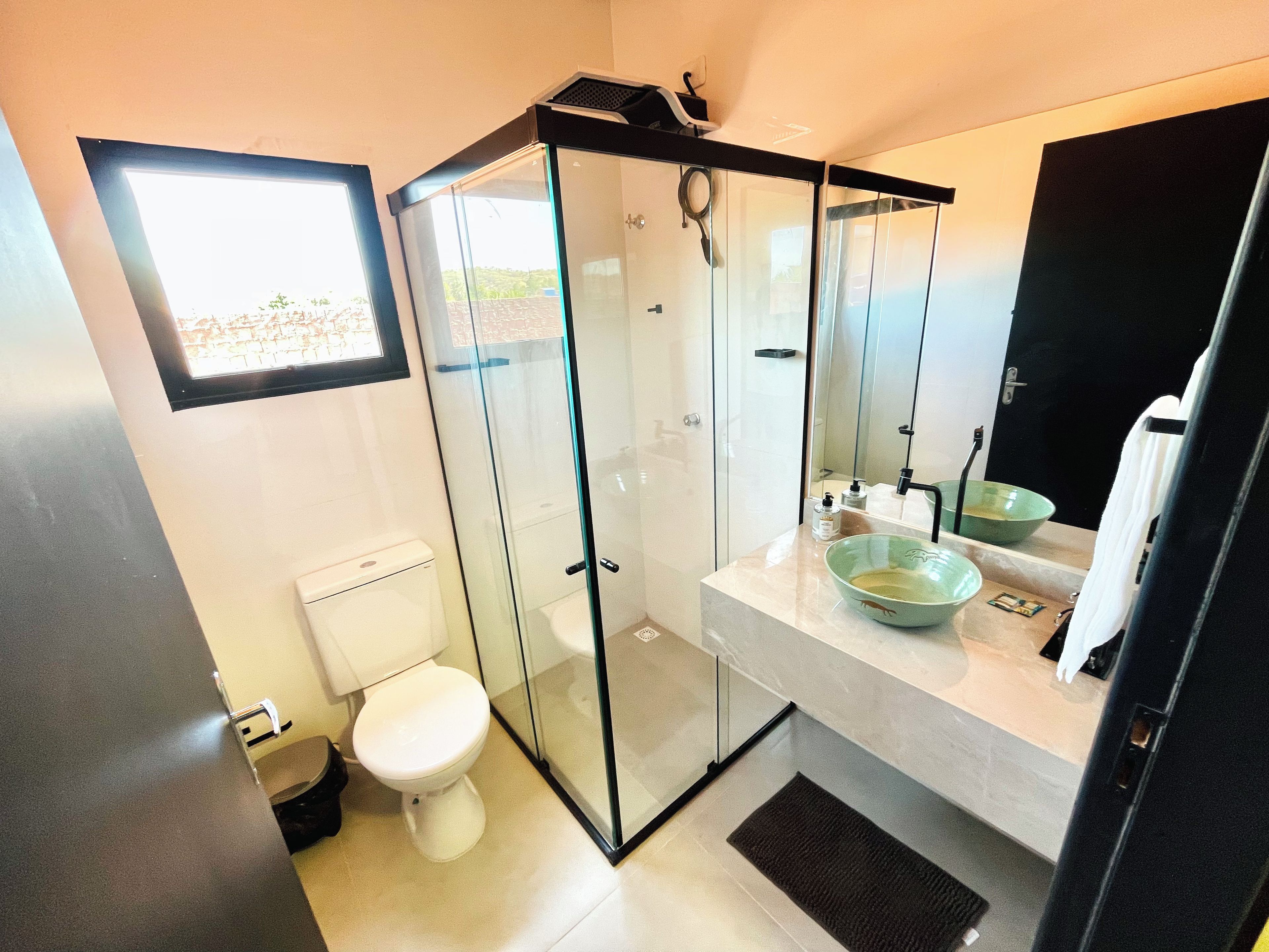 Une salle de bain moderne avec une douche à parois de verre, des toilettes blanches et un lavabo avec un récipient vert.