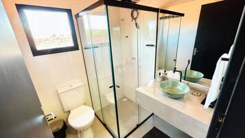 Une salle de bain moderne avec une douche à parois de verre, des toilettes blanches et un lavabo avec un récipient vert.