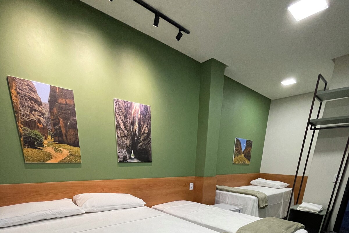 A hotel room with two beds, a bunk bed, a wooden headboard, a green wall, and two framed pictures.