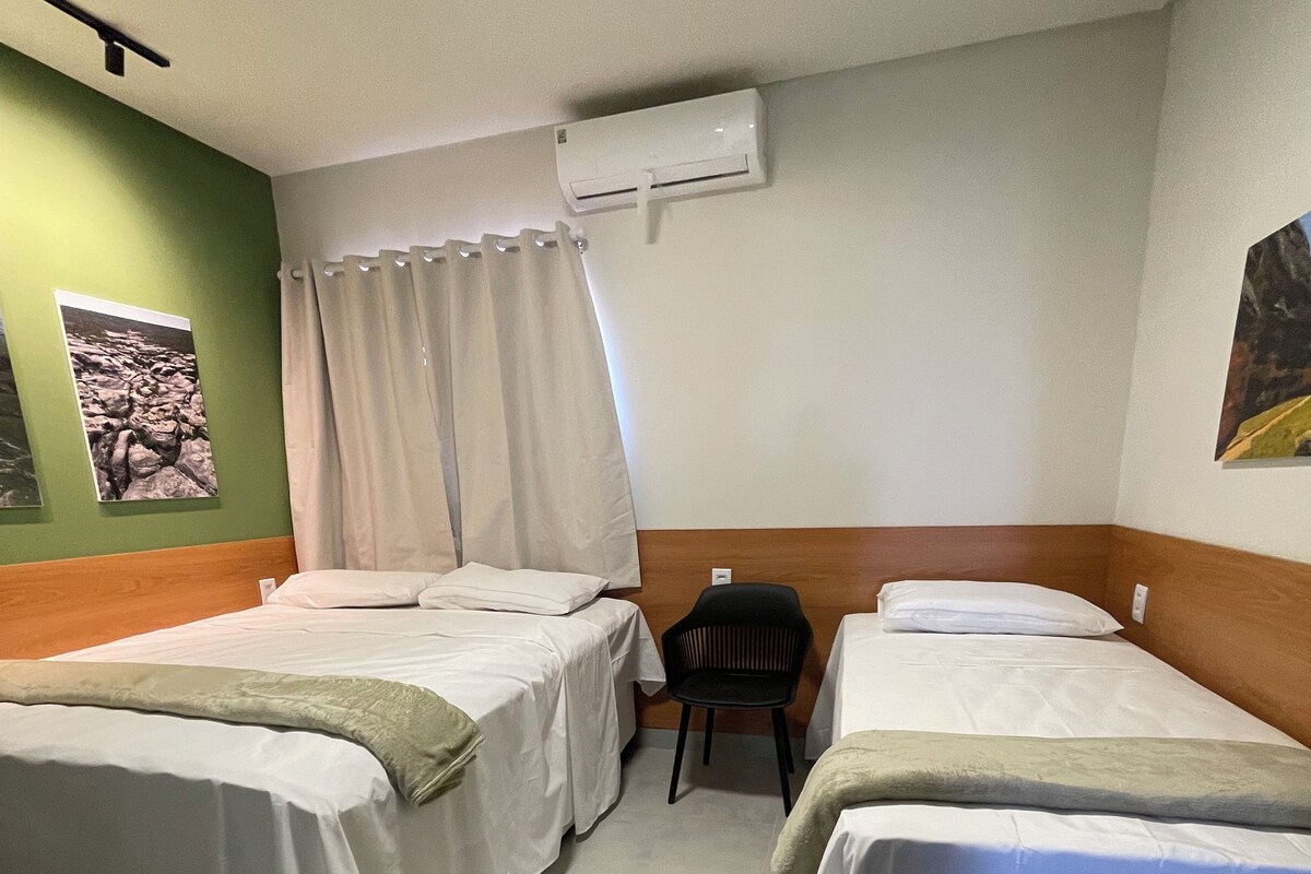 A hotel room with two beds, a chair, an air conditioning unit, and a wall-mounted picture.