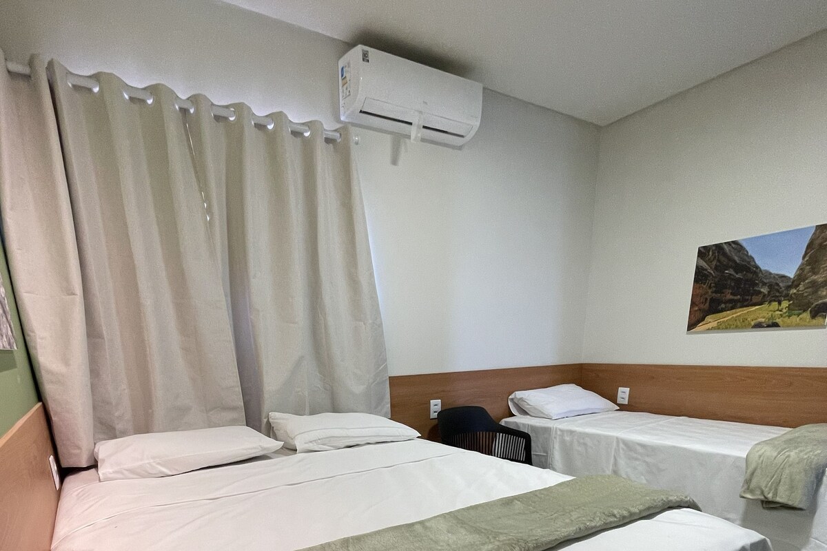 A hotel room with a bed, a chair, a table, and an air conditioning unit.