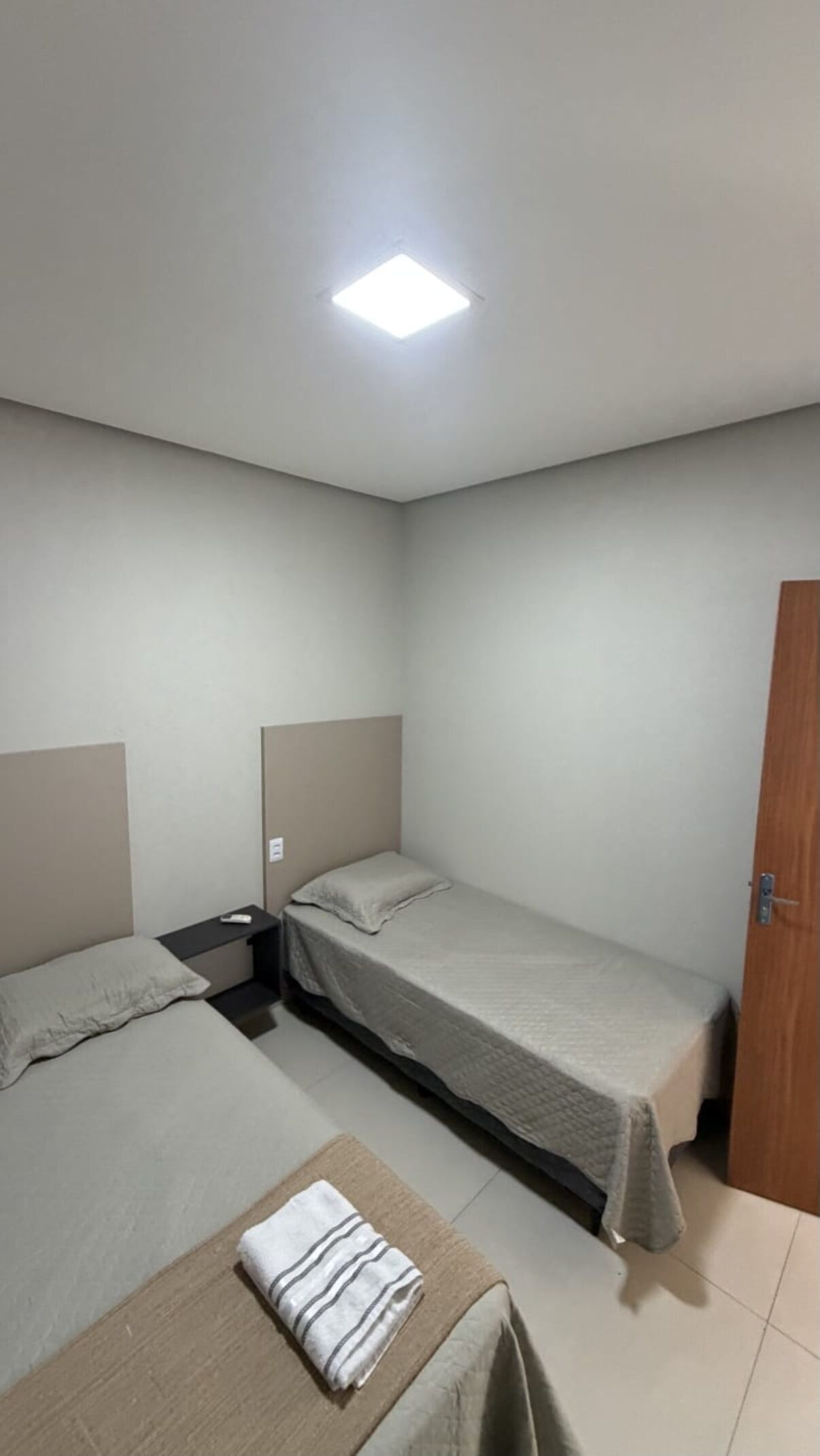 Una habitación pequeña y limpia con dos camas individuales, una mesita de noche y una puerta.