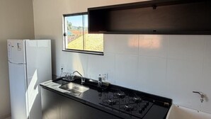 Uma cozinha moderna com fogão a gás embutido, geladeira e janela com vista para um jardim.