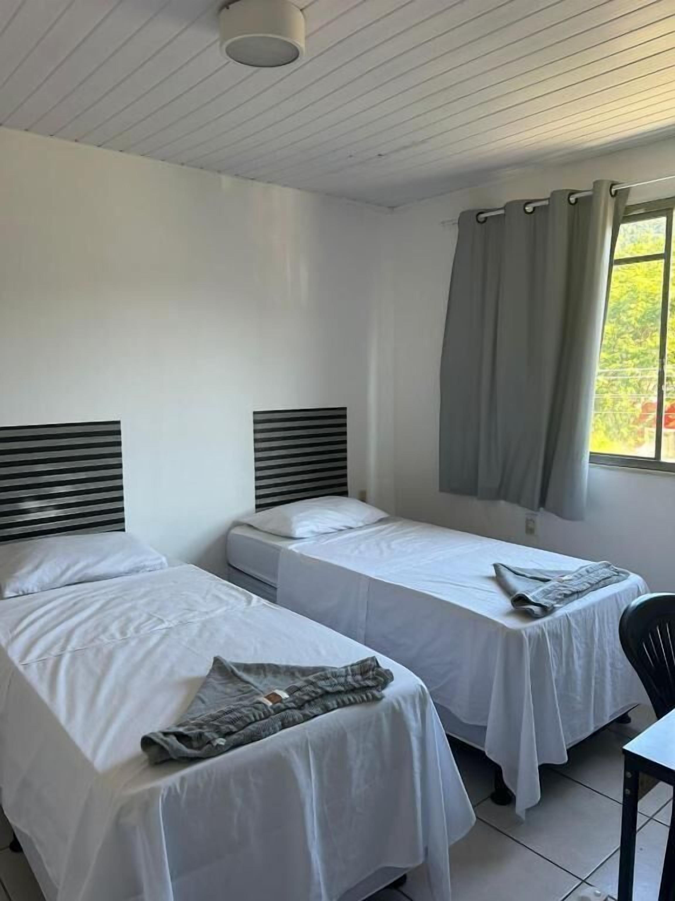 A room with two beds, a table, and a window with curtains.