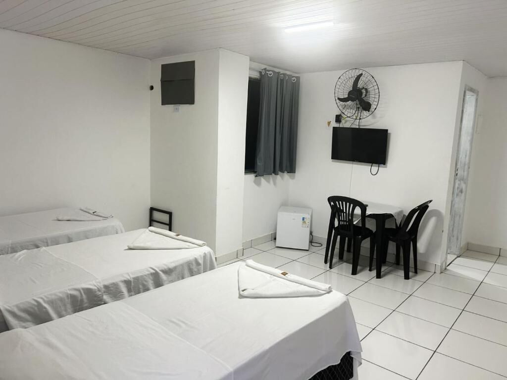 A hotel room with two beds, a desk, a chair, a TV, and a fan.