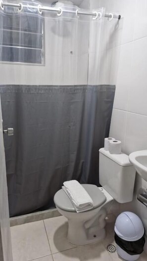 A bathroom with a toilet, a sink, a shower curtain, and a trash bin. - Hotel Balneário (Angra dos Reis)