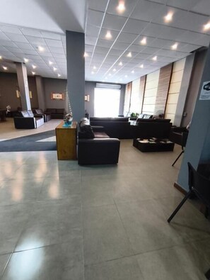 A spacious lobby with a reception desk, seating areas, and a large window providing natural light. - Hotel Balneário (Angra dos Reis)