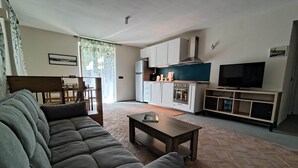A living room with a sofa, a coffee table, a TV, and a kitchen area with cabinets and appliances. - In the shade of a beech tree: An oasis of tranquility just a few minutes from the lake (Miasino)