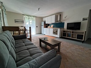 Ein Wohnzimmer mit einer Couch, einem Couchtisch, einem Fernseher und einer Küchenzeile mit Schränken und Geräten.