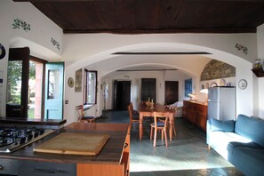 Eine Küche mit Gasherd, einem Holzespeisetisch und Stühlen, einem offenen Durchgang zu einem Essbereich und einem blauen Sofa im Wohnzimmer.