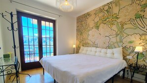 A bedroom with a large bed, a glass table, a door with a view, and a floral wallpaper. - Orta Blu Lake House: Spectacular view of Lake Orta, great (Miasino)