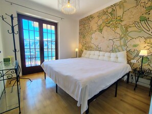 Ein Schlafzimmer mit einem großen Bett, einem Glastisch, einer Tür mit Blick und blumigem Wandpapier.