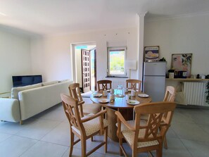 Ein Essbereich mit rundem Tisch, Holzstühlen und einem Fernseher im Hintergrund.