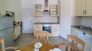 A compact kitchen with white cabinets, a built-in oven, and a dining table with chairs. - Orta Blu Lake House: Spectacular view of Lake Orta, great (Miasino)