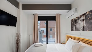A hotel room with a bed, a flat-screen TV, a painting, and a view of buildings outside. - Athens Vein (Athens)