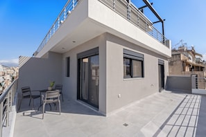 Un edificio moderno con balcón, una mesa con sillas y una planta en maceta.
