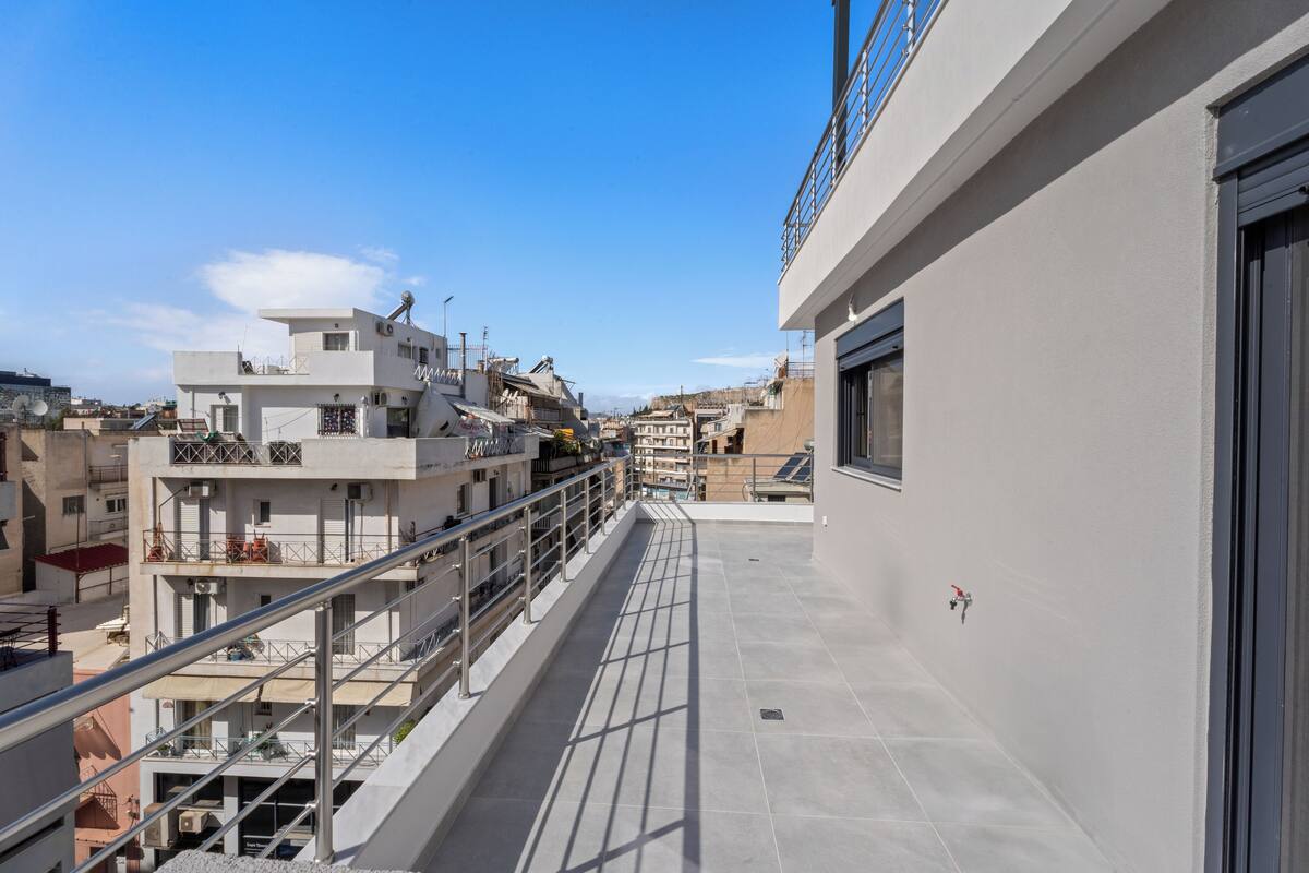 Terraço no telhado com guarda-corrimão de metal, vista de edifícios próximos e céu claro.