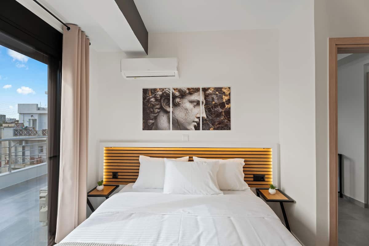 Quarto de hotel moderno com uma cama grande, cabeceira de madeira, vista para a cidade e um quadro na parede.