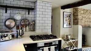 A kitchen with a gas stove, a coffee maker, and hanging utensils. - Cosy Cotswold Cottage with Fireplace and Courtyard (Oxfordshire)