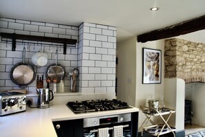 A kitchen with a gas stove, a coffee maker, and hanging utensils.