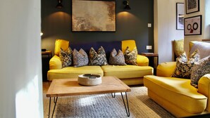 A living room with a yellow sofa set, a wooden coffee table, and a large abstract painting on the wall. - Cosy Cotswold Cottage with Fireplace and Courtyard (Oxfordshire)