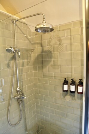 A shower with a handheld showerhead and a wall-mounted faucet, with two bottles of shampoo and conditioner on the wall.