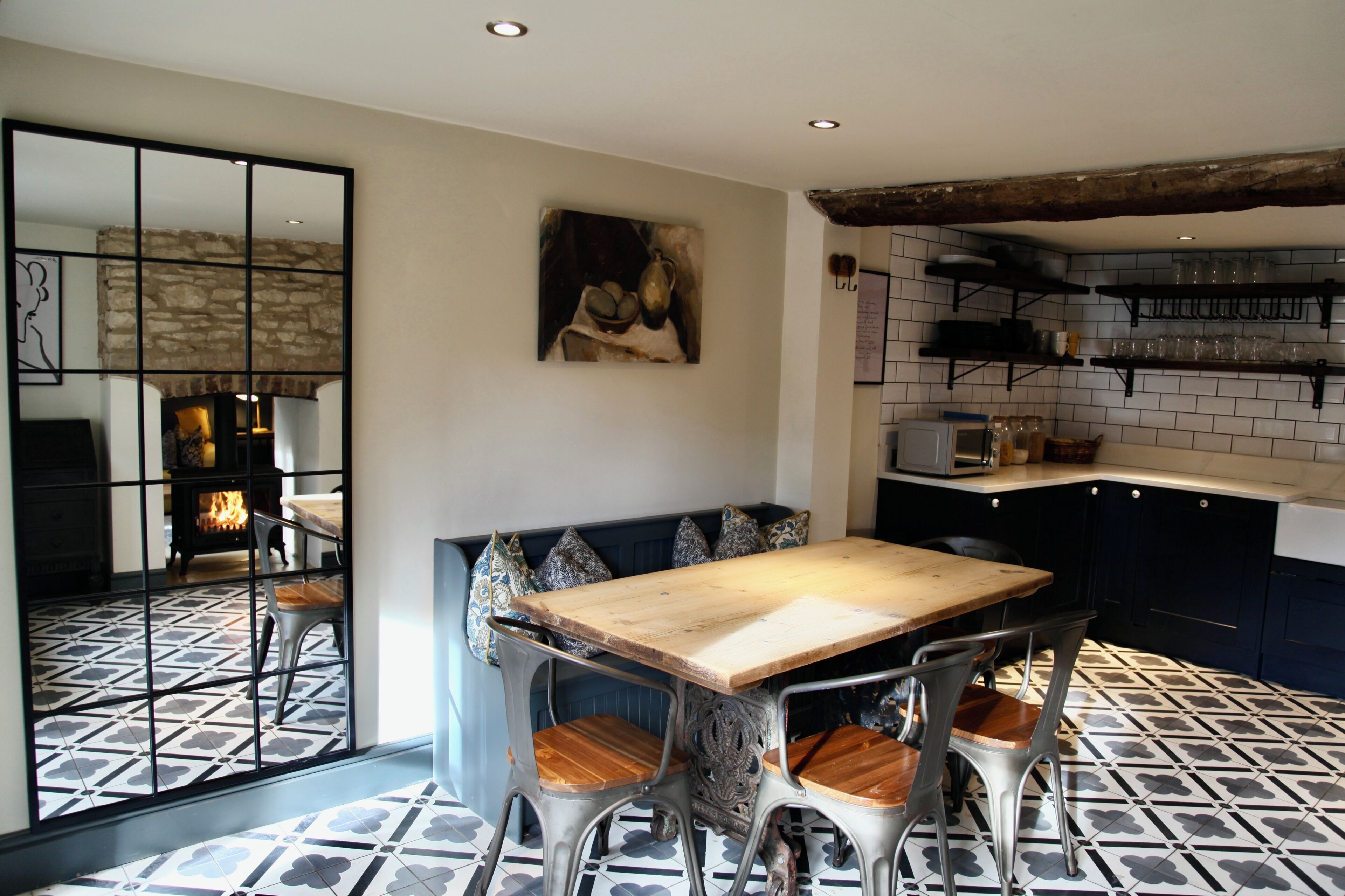 A dining area with a wooden table and metal chairs, a kitchen with shelves, and a stone wall.