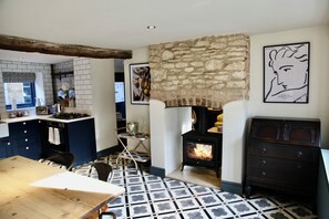 A kitchen with a stone wall, a wood-burning stove, and a tiled floor.