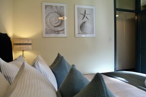A hotel room with a bed, pillows, a lamp, and two framed pictures on the wall.
