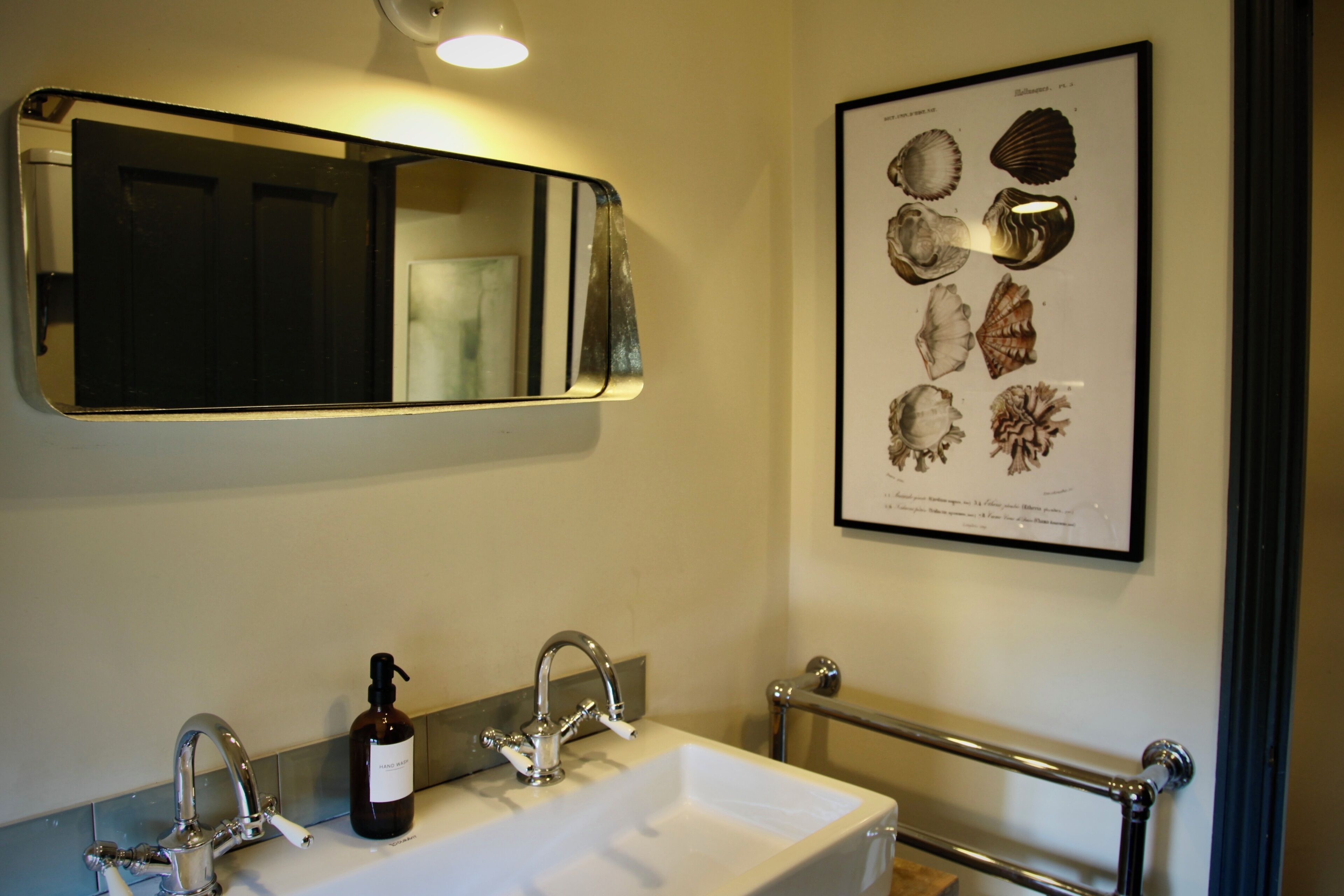 A bathroom with a white sink, two faucets, a framed shell artwork, and a mirror.