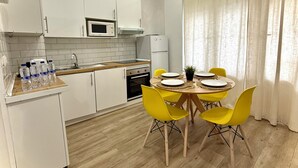 Una cocina moderna con armarios blancos, un microondas y un refrigerador. Hay una mesa de comedor con sillas amarillas y platos para cuatro.