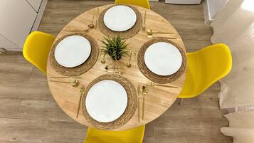 Een ronde eettafel met vier stoelen, een kleine plant en gouden bestek.